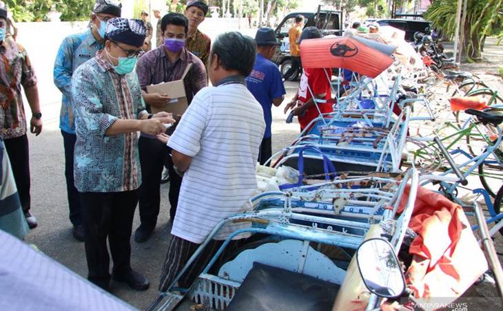 Bupati Banyuwangi Abdullah Azwar Anas (kiri) memberikan bantuan sembako kepada tukang becak di Taman Sri Tanjung, Banyuwangi, Jawa Timur, Kamis (26/3/2020). ANTARA/Budi Candra Setya/hp.