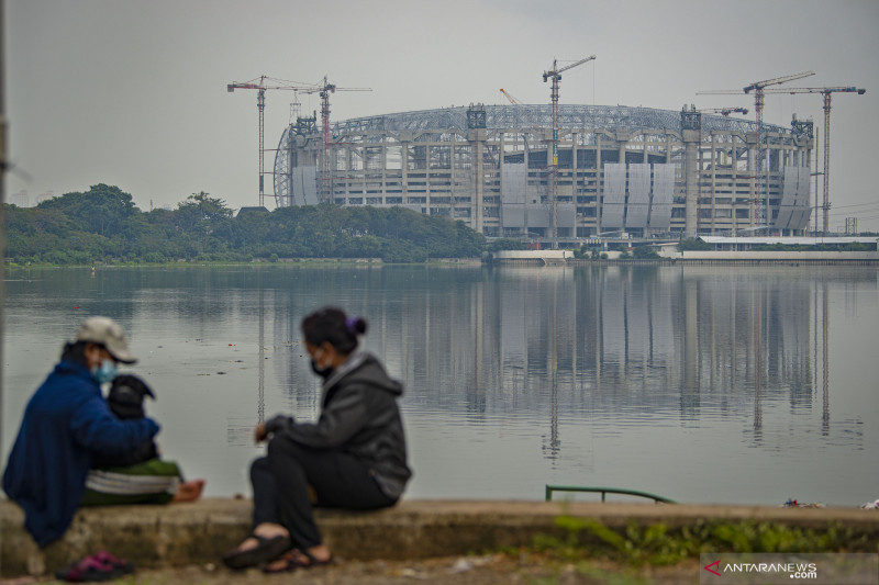 Sejumlah warga bercengkerama dengan latar belakang proyek pembangunan Jakarta International Stadium (JIS) di tepi Danau Cincin, Papanggo, Tanjung Priok, Jakarta, Sabtu (24/7/2021). Berdasarkan laporan mingguan ke-98 yang dirilis 20 Juli 2021, PT Jakarta Propertindo (Jakpro) mencatat realisasi pembangunan stadion yang diproyeksikan berkapasitas 82 ribu penonton itu telah mencapai 63,97 persen. ANTARA FOTO/Aditya Pradana Putra/wsj.
