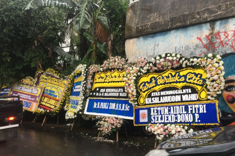 Karangan bunga belasungkawa atas meninggalnya Salahuddin Wahid (Gus Sholah) yang dibasahi air hujan saat rombongan pengantar jenazah bergerak dari depan gang menuju rumah duka yang terletak di Mampang, Jakarta Selatan, Senin (3/2/2020). (ANTARA/ Abdu Faisal)