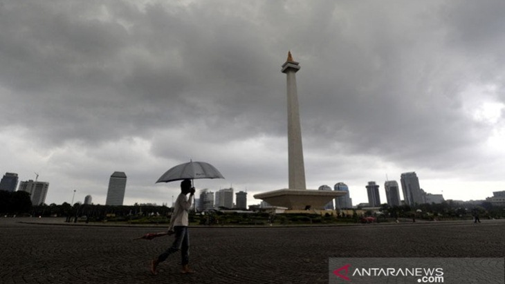 Pria berpayung berjalan saat awan mendung menggelayut di atas kawasan Monumen Nasional (Monas), Jakarta Pusat, Kamis (13/6). (ANTARAFOTO/ANDIKA WAHYU)