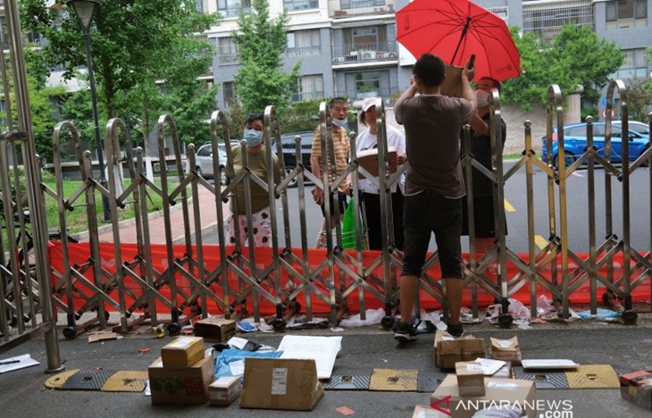 Seorang kurir menyerahkan bingkisan kepada seorang warga dari atas pagar jalan, di Beijing, China, Senin (29/6/2020). REUTERS/Tingshu Wang/WSJ/cfo