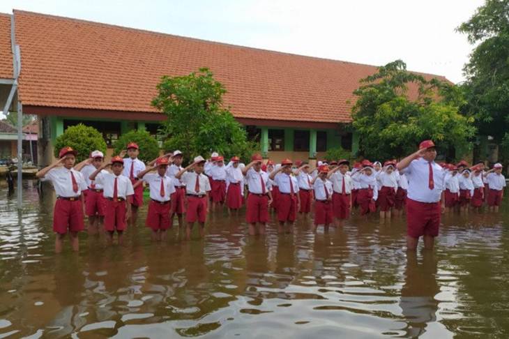 Siswa SDN Banjarasri melaksanakan upacara bendera di tengah banjir yang melanda halaman sekolah mereka. (Antarajatim/SO/IS)