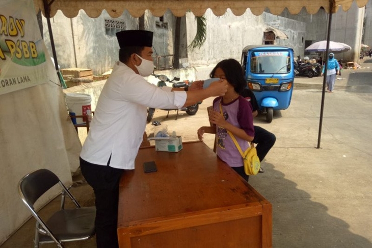 Petugas di Posko PSBB Pasar Kebayoran Lama memberikan masker kepada seorang anak yang sedang melintas, sesuai aturan Pembatasan Sosial Berskala Besar (PSBB) mewajibkan setiap orang menggenakan masker saat berada di luar ruangan, Jumat (22/5/2020) (ANTARA/HO-Camat Kebayoran Lama)