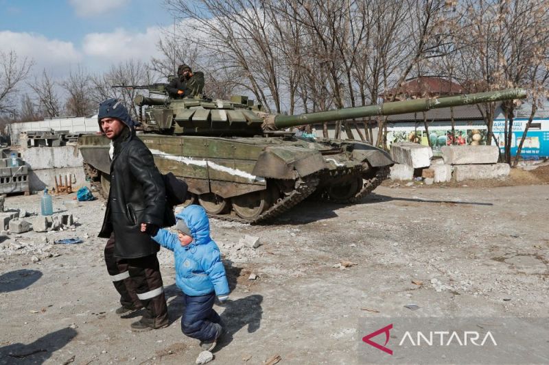 Seorang warga berjalan dengan seorang anak melewati tank pasukan pro-Rusia selama konflik Ukraina-Rusia di kota pelabuhan Mariupol yang terkepung, Ukraina, 18 Maret 2022. (ANTARA/Reuters/Alexander Ermochenko/as)