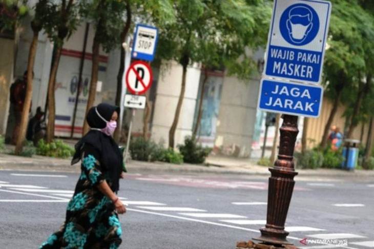 Seseorang melintas di depan rambu peringatan wajib pakai masker dan jaga jarak terpasang di Jalan Tunjungan Surabaya. (ANTARA Jatim/Didik Suhartono)