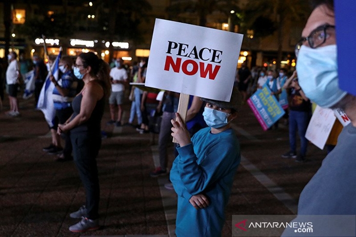 Seorang demonstran yang mengenakan masker pelindung memegang poster saat protes bersama ratusan warga lainnya menentang rencana aneksasi Israel atas wilayah Palestina di Tepi Barat yang didudukinya, dan tentang masalah pengangguran dan ekonomi, di Tel Aviv, Israel (23/6/2020) waktu setempat. ANTARA/REUTERS/Ammar Awad/aa.