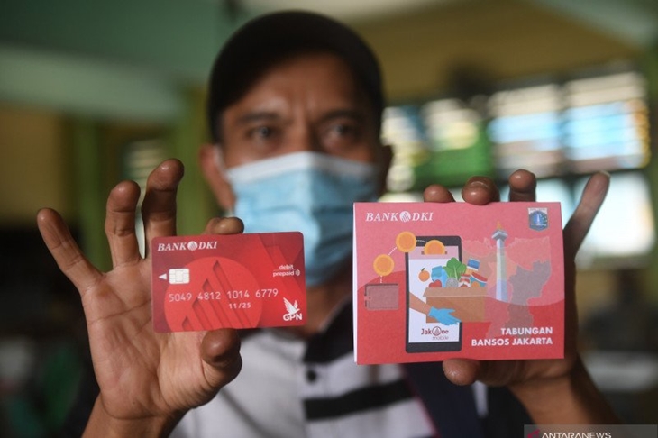 Warga menunjukan buku tabungan dan kartu debit usai mengambil Bantuan Sosial Tunai (BST) di SMAN 111, Jakarta, Selasa (19/1/2021). Pemprov DKI Jakarta menyalurkan BST sebesar Rp300 ribu per KK kepada 1.055.216 KK mulai Januari hingga April 2021. ANTARA FOTO/Akbar Nugroho Gumay/wsj.