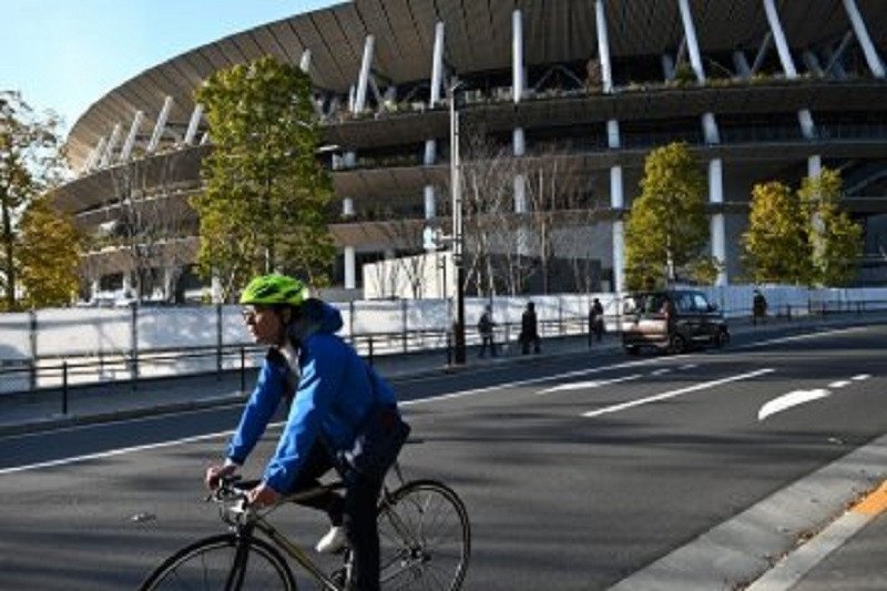 Seorang pesepeda mengayuh sepedanya dalam foto tertanggal 11 Februari 2021 di luar Stadion Nasional yang menjadi venue utama acara pembukaan dan penutupan Olimpiade Tokyo 