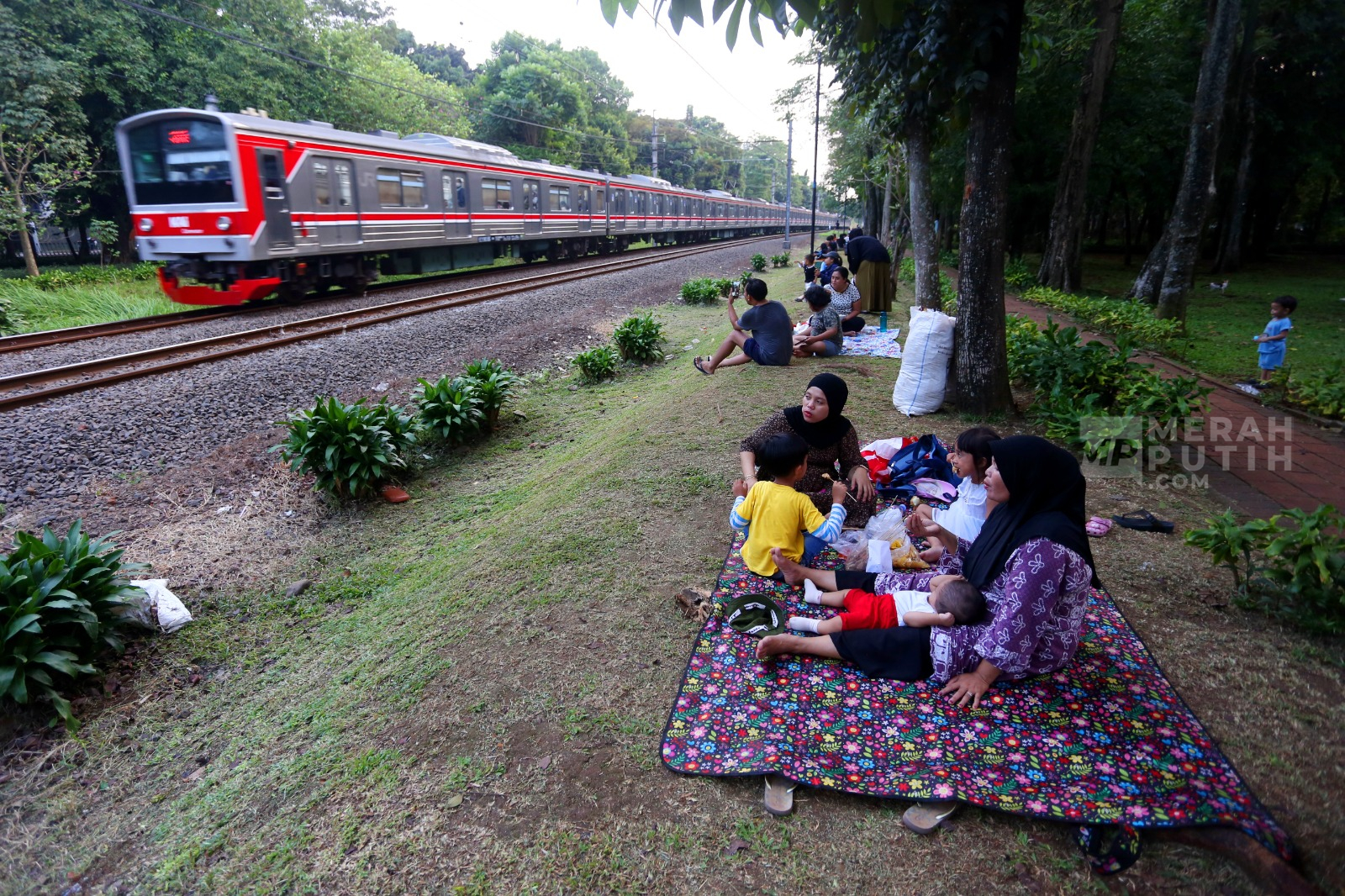 Libur Akhir Pekan, Warga Piknik Sambil Menikmati Lalu Lalang KRL di Taman Tanah Kusir