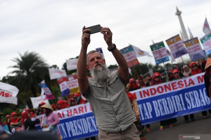  Wisatawan mancanegara berswafoto dengan latar belakang buruh yang mengikuti aksi memperingati Hari Buruh di kawasan Patung Kuda Jakarta, Rabu (1/5/2019). (Antara Foto/ Wahyu Putro A)