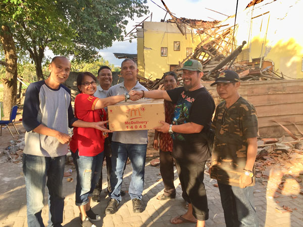 Warga menerima bantuan dengan latar belakang bangunan yang runtuh akibat gempa